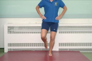 Photograph of person with hands on their waist keeping one leg straight and raising the other at the knee