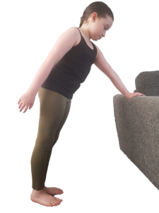 Child leaning forward with one hand on the back of a sofa, the other hand swinging backwards away from the sofa at their side