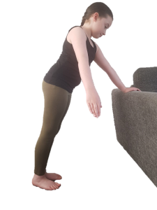 Child leaning forward with one hand on the back of a sofa, their free hand is swinging sideways across their body