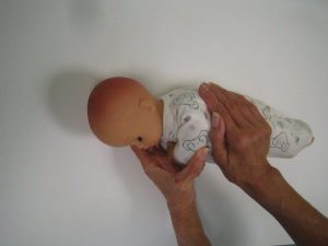 Photograph of baby laid on its side with someone supporting it's neck, and using their other cupped hand to press onto the baby's side