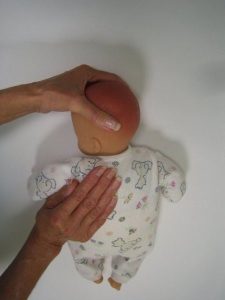 Photograph of baby laid on their front with someone supporting their neck and using their other cupped hand to press into their back
