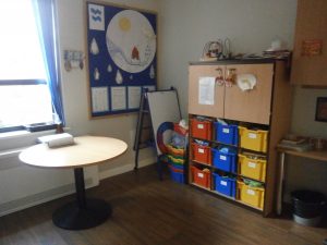 Classroom with a table, coloured bins, a whiteboard, and a window